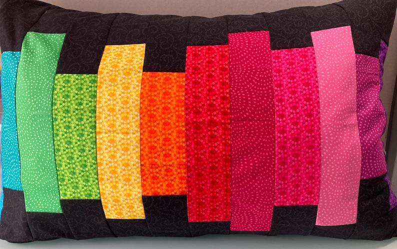 May include: A rectangular decorative pillow with a black background and vertical stripes of various colors. The stripes include turquoise, green, yellow, orange, red, pink, and purple. The stripes have different patterns, and the pillow is likely for home decor.