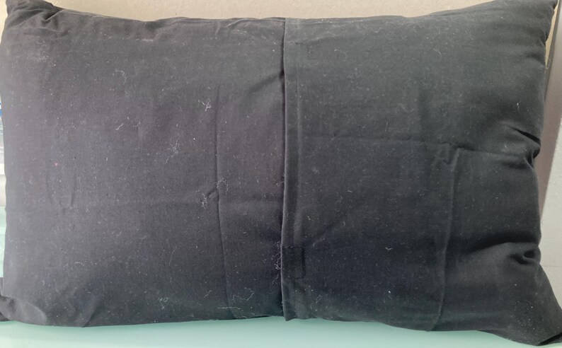 May include: A rectangular black pillow with a seam down the middle. The pillow is made of a dark fabric and appears to be filled with a soft material. The pillow is designed for comfort and support.