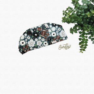 May include: A scrub cap featuring a dark teal background with a repeating pattern of white flowers, brown footballs, and black football helmets. A small white tag with the text Sunday Thread Club is attached to the side of the fabric head covering.