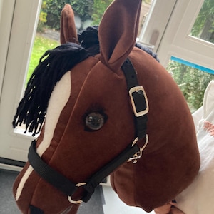 May include: A brown plush horse head with a black mane and a white stripe down the face. It features a black halter with silver-colored hardware and a realistic eye. This toy is designed for imaginative play.