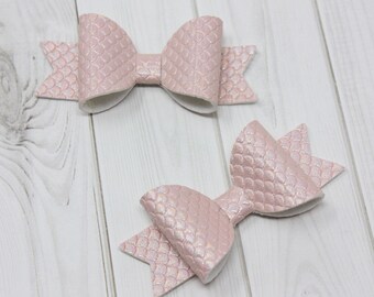 May include: Two pink hair bows with a shimmery finish. The bows are made of a textured fabric that resembles fish scales.