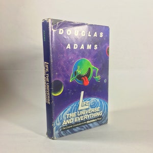 Könnte beinhalten: Ein gebundenes Buch mit dem Titel "Life, The Universe and Everything" von Douglas Adams. Das Cover zeigt eine lila Weltraumszene mit einer grünen Cartoonfigur und dem Titel in Weiß. Der Buchrücken trägt ebenfalls den Titel.
