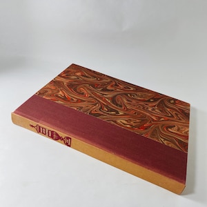 May include: A hardcover book with a marbled cover in shades of brown, red, and cream. The spine is a deep red color with gold lettering and decorative elements. The book's title is "Man and Superman" by G.B. Shaw.