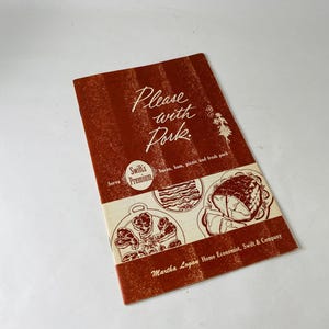 Könnte beinhalten: Ein Vintage-Kochbuch mit dem Titel "Please with Pork" in Rot- und Cremefarben. Das Cover zeigt Illustrationen von Schweinefleischgerichten und den Text "Swift's Premium". Autorin ist Martha Logan.