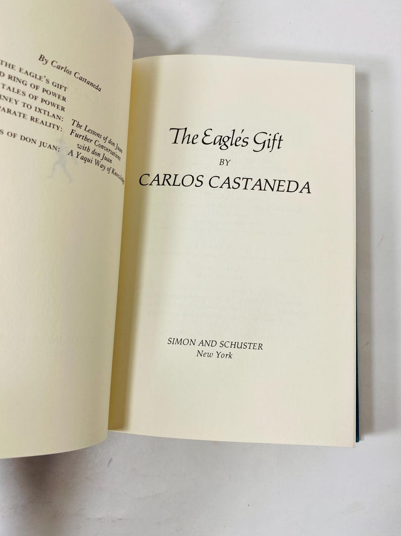 Op de afbeelding: Een open boek met de titel "The Eagle's Gift" van Carlos Castaneda. Het boek heeft cr&egrave;mekleurige pagina's met zwarte tekst. De naam van de uitgever, Simon and Schuster, en New York staan onderaan de pagina.