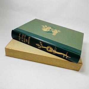 May include: A green hardback book with gold lettering titled "On the Origin of Species" by Charles Darwin. The book is sitting on a wooden box.