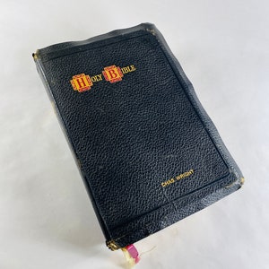 May include: A black leather-bound Holy Bible with gold lettering and the words "HOLY BIBLE" on the front cover. The book is closed and has a worn, vintage look. The text "CHAS WRIGHT" is printed in gold on the bottom right corner of the cover.