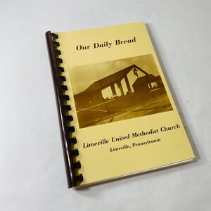 Könnte beinhalten: Ein spiralgebundenes Buch mit dem Titel "Our Daily Bread" mit einem sepiafarbenen Bild einer Kirche. Der Einband ist hellgelb und der Text "Limeville United Methodist Church" ist darunter gedruckt.
