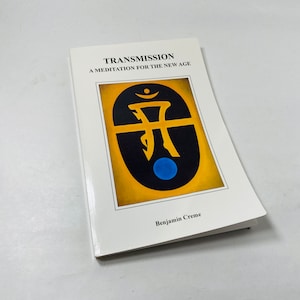 May include: A white book with the title "Transmission: A Meditation for the New Age" and a black and yellow symbol with a blue circle in the center. The author is Benjamin Creme.