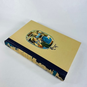 May include: A vintage hardcover book with a yellow cover and a blue spine. The cover features an illustration of a family gathered around a table, with a woman holding a large bowl. The book title is "The Little House on the Prairie" by Laura Ingalls Wilder.