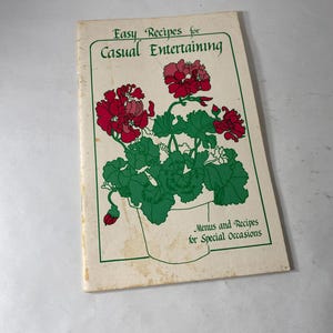 May include: A vintage cookbook titled "Easy Recipes for Casual Entertaining." The cover features a floral illustration of red geraniums in a white pot with green leaves. The book also includes menus and recipes for special occasions.