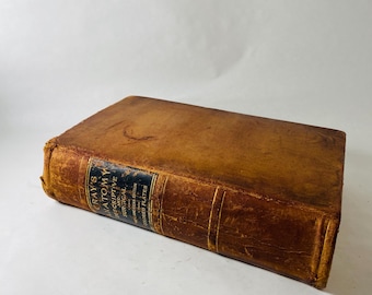 May include: A vintage leather-bound book titled Gray's Anatomy Descriptive and Surgical, American Edition, Colored Plates. The book features a worn, tan-coloured leather cover with a black rectangular label on the spine containing gold text.