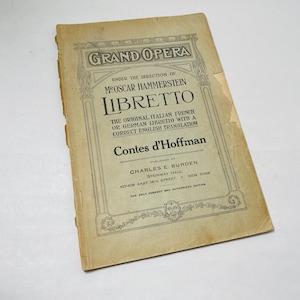 May include: A vintage program for the opera "Contes d'Hoffman" by Jacques Offenbach. The program is printed on yellowed paper and features a decorative border. The text reads "Grand Opera" and "Under the Direction of Mr. Oscar Hammerstein".