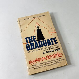 May include: A vintage paperback book titled "The Graduate" by Charles Webb. The cover features a silhouette of a person in a graduation cap and gown, with the title in bold blue letters. The book is a "Bestseller - 19th Big Printing."