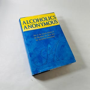 May include: A book titled "Alcoholics Anonymous" with a blue cover and yellow text. The cover also includes the text "This is the Fourth Edition of the Big Book, the Basic Text for Alcoholics Anonymous."