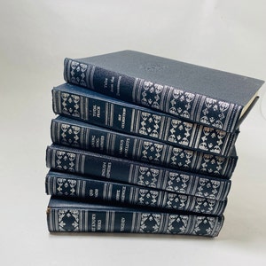 May include: A stack of nine blue hardcover books with silver lettering and decorative designs on the spines. The titles include "Total Peace", "Living Biographies", "Famous Novelists", "English Comedies", "1000  Aphorisms", "Henryk Sienkiewicz", "Turgenev", "The Best Known Works", and "Tales from the Decameron".