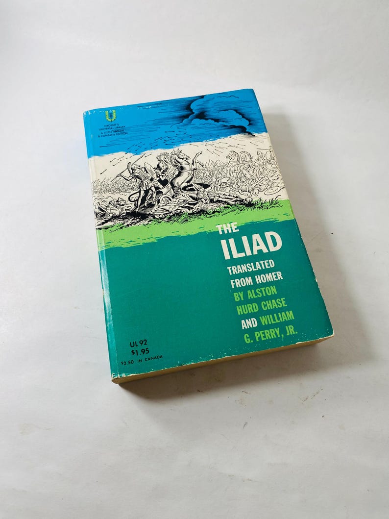 K&ouml;nnte beinhalten: Ein Vintage-Taschenbuch mit dem Titel "The Iliad". Das Cover zeigt einen blauen Himmel und ein gr&uuml;nes Band mit dem Titel in Wei&szlig;. Die Illustration auf dem Cover zeigt eine Kampfszene in Schwarzwei&szlig;.