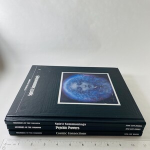 May include: A stack of black books titled "Spirit Summonings," "Psychic Powers," and "Cosmic Connections." The top book features a blue and white image of a face. The books are part of the "Mysteries of the Unknown" series.
