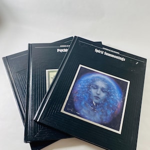 May include: Three black hardcover books with the titles "Mysteries of the Unknown" and "Spirit Summonings" visible. One book features a blue and white image of a woman's face. The books are stacked on a white surface.