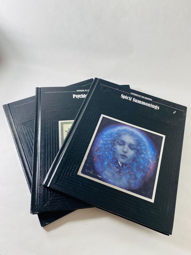 May include: Three black hardcover books with the titles "Mysteries of the Unknown" and "Spirit Summonings" visible. One book features a blue and white image of a woman's face. The books are stacked on a white surface.