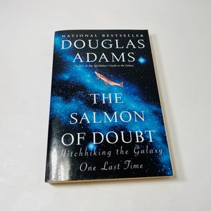 Könnte beinhalten: Ein Buch mit dem Titel "The Salmon of Doubt" von Douglas Adams. Das Cover zeigt einen blauen und schwarzen Hintergrund mit einem Lachs. Der Text lautet "National Bestseller" und "Hitchhiking the Galaxy One Last Time".