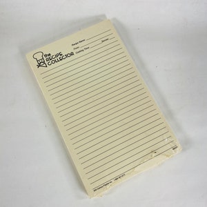 May include: A white notepad with lined pages for writing down recipes. The notepad has a black logo that says "The Recipe Collector" with a chef's hat and mustache.