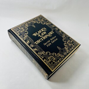 May include: Black leather-bound book with gold lettering and ornate design. The title is "Black's Law Dictionary" with the words "Special Deluxe Fifth Edition" below.