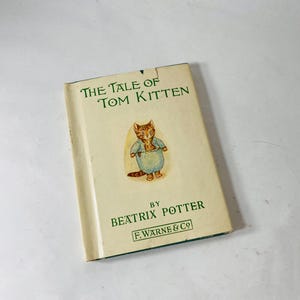 May include: A vintage copy of "The Tale of Tom Kitten" by Beatrix Potter. The book has a cream-colored cover with green text and an illustration of a cat wearing a blue outfit. The book is from F. Warne & Co.