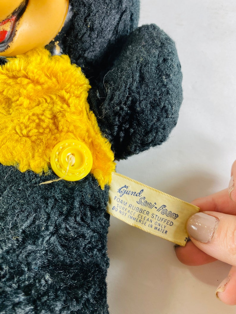 May include: Black and yellow plush toy with a button on the chest. The toy has a tag that reads "Gund Sani-Foam Foam Rubber Stuffed Surface Clean Only Do Not Immerse In Water".