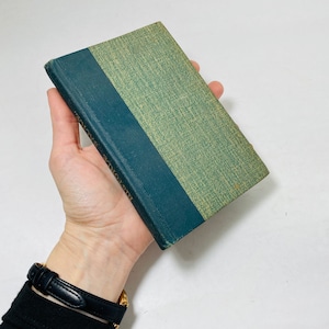 Puede incluir: Un libro de tapa dura verde y azul con el título "The Adventures of Tom Sawyer" en el lomo.