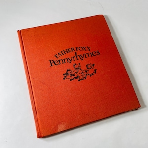 May include: A vintage book titled "Father Fox's Pennyrhymes" with an orange cover. The title and illustrations of foxes are in black. The book is closed and slightly angled, showing its cover.