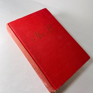 May include: A red hardback book with gold lettering reading "Mrs. B" on the cover. The book has a textured surface and appears vintage. The spine is visible, with faded text.