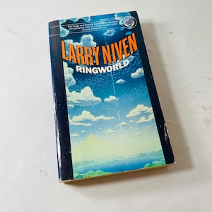 May include: A paperback book titled Ringworld by Larry Niven with a dark blue cover featuring a bright blue sky, white clouds, and a green landscape. The text reads: The Hugo and Nebula Award winning novel, the gripping story of a ring-shaped world around a distant sun.
