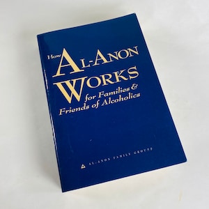 May include: A blue book titled "How Al-Anon Works for Families & Friends of Alcoholics" with a gold triangle and the text "Al-Anon Family Groups" on the bottom.
