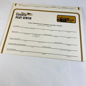 May include: A Cessna Pilot Center Flight Instructor Training Record Folder for new FAR Part 141 schools. The folder has sections for pilot information, school dates, medical certificate, radiotelephone operator permit, and pilot certificate.