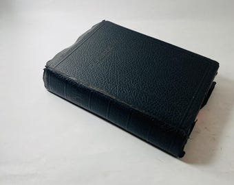 May include: A closed, black book with a textured cover. The book is rectangular and appears to be leather-bound. The edges of the book are slightly worn, suggesting age or use. The background is plain white.