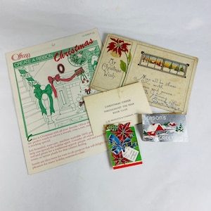 Könnte beinhalten: Eine Sammlung von Vintage-Weihnachtskarten und -dekorationen. Die Karten zeigen einen Weihnachtsstern, eine Winterszene und einen Weihnachtsgruß. Die Dekorationen umfassen ein kleines Buch mit einer Weihnachtsbotschaft und einen silbernen Anhänger mit einem Haus und einem Weihnachtsbaum.