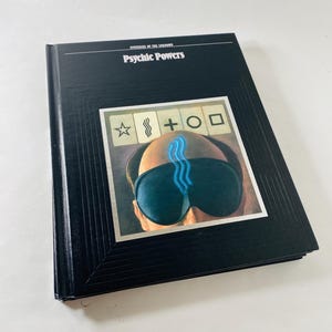 May include: A hardcover book titled "Mysteries of the Unknown: Psychic Powers." The cover is black with the title in white. The image on the cover features a person wearing a sleep mask with blue lines and symbols.