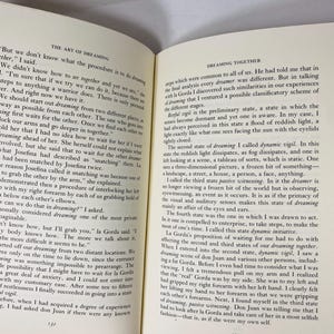 Op de afbeelding: Open boek met tekst over dromen en de kunst van het dromen. De pagina's zijn vergeeld en de tekst is zwart. Het boek is open op een dubbele pagina, met tekst die beide pagina's vult. Het boek ligt op een wit oppervlak.