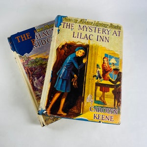May include: Two vintage paperback books, one titled "The Mystery at Lilac Inn" by Carolyn Keene, featuring a girl in a blue dress peeking around a door, and the other titled "The Haunted Ridge" with a blue cover.