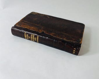 May include: An antique leather-bound book with a dark brown cover. The spine features gold lettering that reads Muret's Rites of Funeral Ancient and Modern, with the year 1683 printed at the bottom. The book shows signs of age and wear.