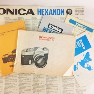 Peut inclure: Une collection de manuels et de brochures d'appareil photo vintage pour l'appareil photo Konica Autoreflex T. Les manuels sont en plusieurs langues, dont l'anglais, l'allemand, le français et l'espagnol. Les brochures présentent une carte du monde et un gros plan de l'appareil photo.