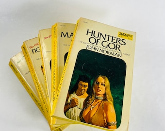 May include: A stack of eight paperback books with yellow covers and black text. The top book is titled "Hunters of Gor" and is the eighth book in the "Saga of Tarl Cabot" series by John Norman. The books are all part of the "Gor" series.