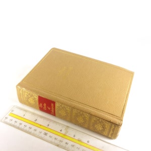 May include: A hardcover book titled "The Works of Shakespeare" with a tan cover and gold embossed details. A clear ruler is placed next to the book, showing measurements in inches.