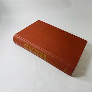 May include: A vintage book with a burnt orange cover. The title "SYBIL" is embossed in gold lettering on the spine. The book is closed and resting on a white surface.