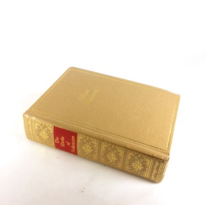 May include: A hardcover book titled "The Works of Shakespeare." The book has a tan cover with gold lettering and decorative patterns. The spine features a red label with white text. The book is closed and resting on a white surface.