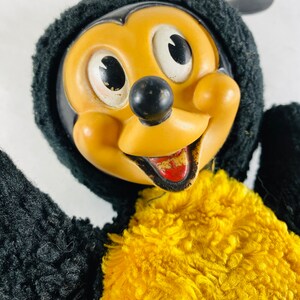 May include: Vintage plush Mickey Mouse toy wearing a black fuzzy hat and yellow fuzzy vest. The toy has a plastic face with black eyes, a black nose, and a red mouth.