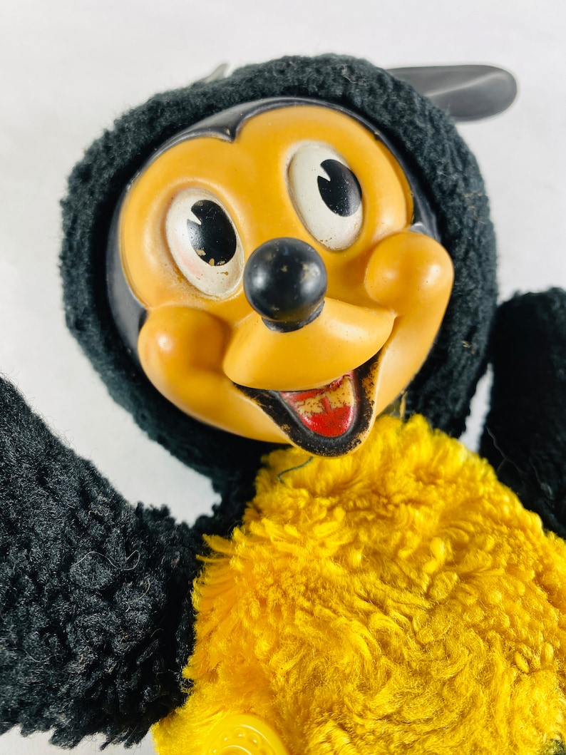 May include: Vintage plush Mickey Mouse toy wearing a black fuzzy hat and yellow fuzzy vest. The toy has a plastic face with black eyes, a black nose, and a red mouth.