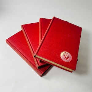 May include: A set of four red hardcover books with a gold-colored design on the front cover. The design features a stylized image of a person wearing a helmet.