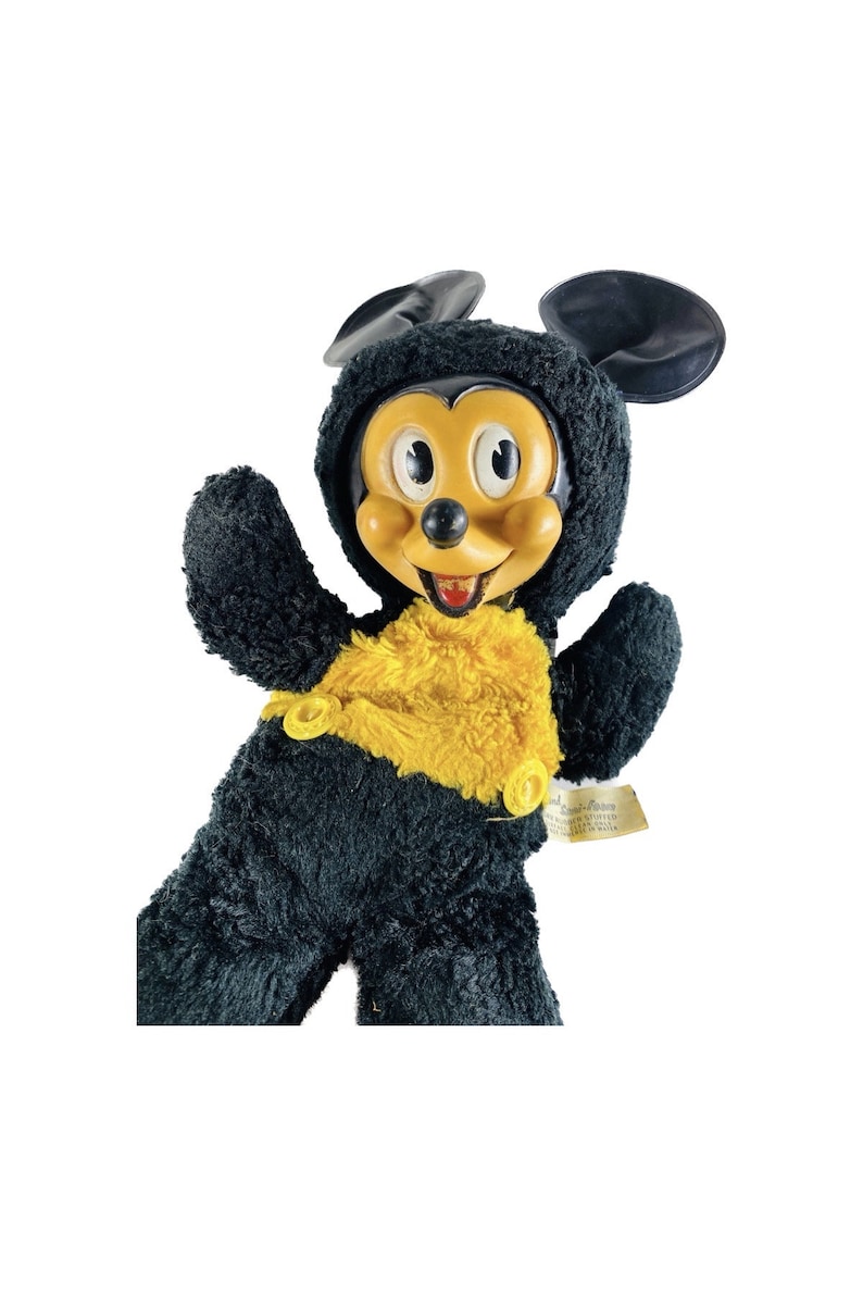 May include: Vintage black and yellow plush Mickey Mouse toy with a plastic face and a tag that reads "Disneyland Stuffed Toys Made in Hong Kong".
